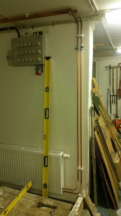 Kopparledningar fastsatta med två klammer vid en vägg med en vattenpass som kontrollerar lodrät linje.