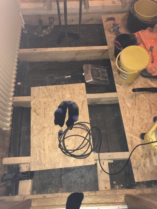 Golvrenovering i badrum med exponerade reglar, OSB-skivor, verktyg och byggmaterial synliga på underlaget.