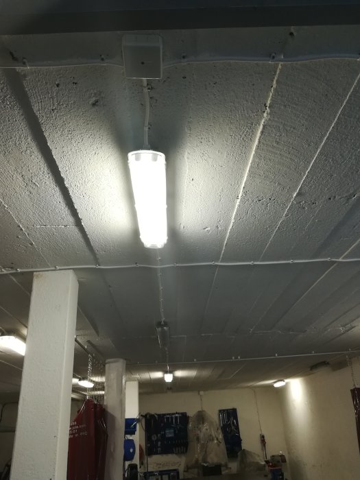 Lampa i taket lyser medan andra lampor är släckta i ett garage med oregelbunden belysning.