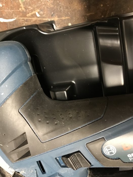 Del av ett verktyg med modifierad plastkomponent, dammpartiklar synliga, på en verkstadsbänk.