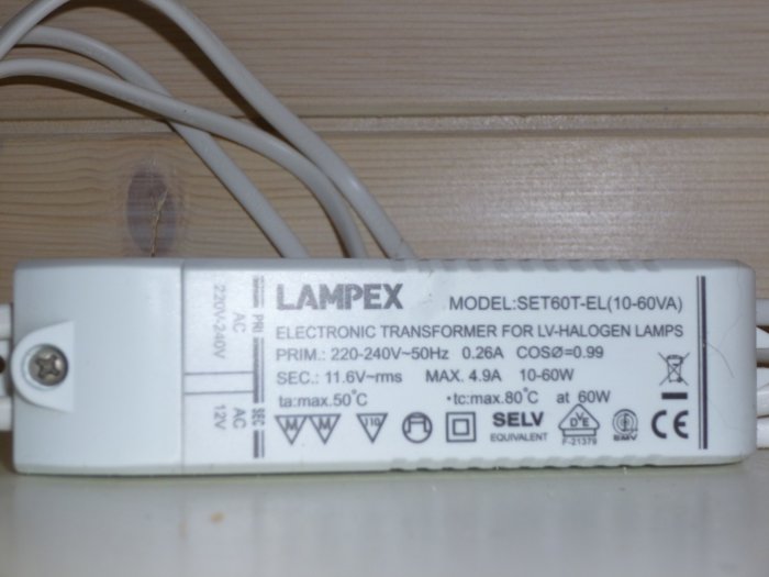 Elektronisk transformator för lågvolts-halogenlampor på en hylla, omgiven av vit elkabel.