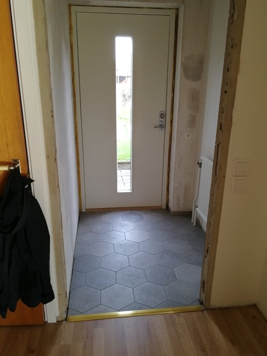 Renoverad ingång med nyinstallerad ytterdörr med fönster och nytt klinkergolv, oslipade väggar.