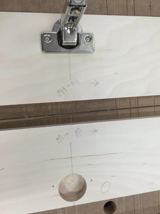 Trästycken med uppmätt och påbörjat fräsarbete för hängningar, markerat med penna, i en dörrtillverkningsprocess.