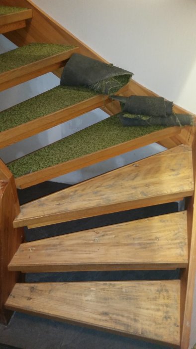 Trætrappe fra 70'erne med grøn tæppebelægning, hvor det tredje trin fra toppen har løse tæppestykker og behøver vedligeholdelse.