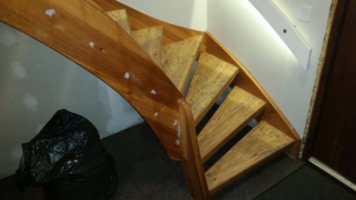 Trætrappe med smalle trin, især det tredje trin er skævt og kan muligvis knirke. En skraldepose ses ved siden af trappen.