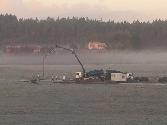 Byggarbetsplats med maskiner och arbetare, arbete pågår i dimmig miljö vid husbygge.