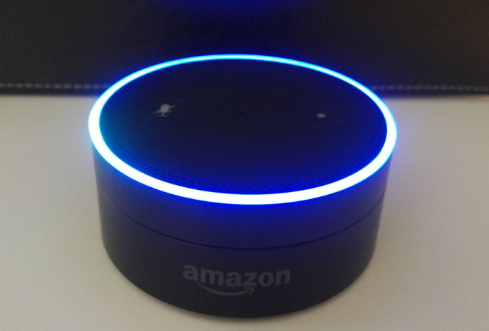 Amazon Alexa Echo Dot smart assistent med aktiv blå ljusring på bord.