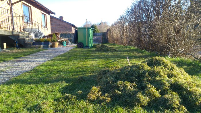 Högar av vertikalskuret gräs på en gräsmatta med en trädgårdsvagn och hus i bakgrunden.