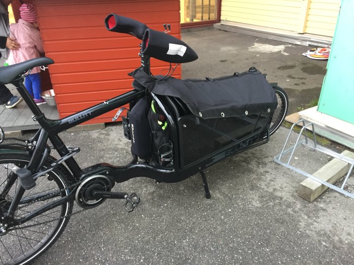 Svart lådcykel parkerad, med fokus på den stängda förvaringslådan fram.