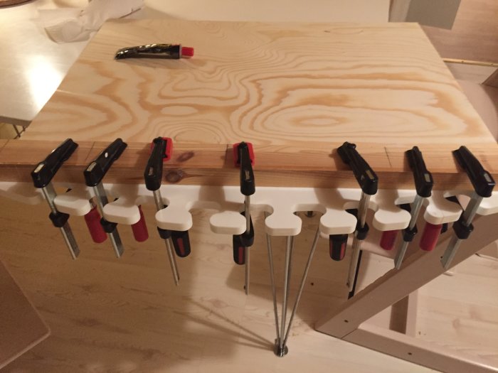 Plywoodskiva fäst med flera klämmor på ett arbetsbord, hantverksprojekt i process.