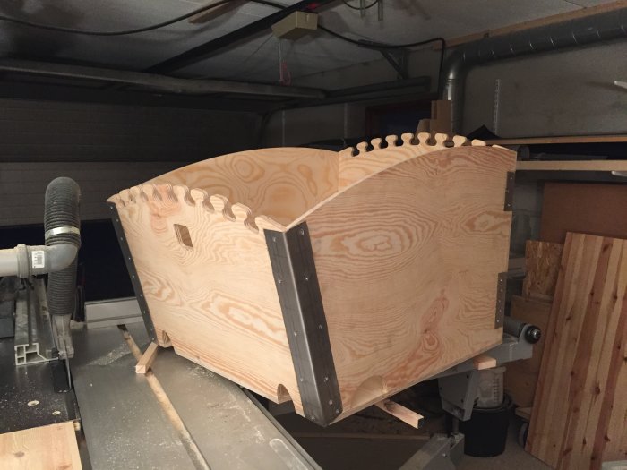 Hörnskydd i plywood med utskurna notcher och metallförstärkning i en verkstadsmiljö.