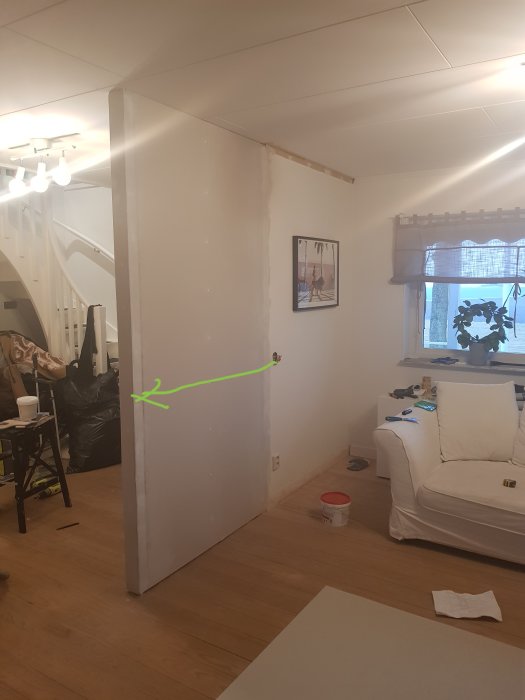 Vardagsrum under renovering med en markerad strömbrytarplats på en ofärdig vit vägg.