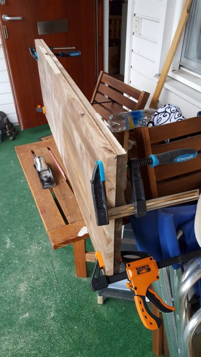 Träskiva fastklämd på arbetsbänk med styrskena och klämmor, redo för limning efter kapning.