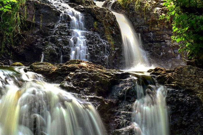 Ett stilla vattenfall omgivet av gröna växter och klippor.