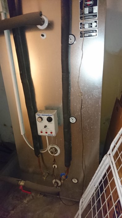 Värmepannans anslutningar och reglage med rör och termometer på väggen.