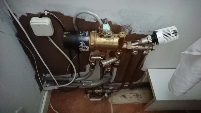 Radiatorkoppling med termostat, rör och ventiler monterade på en vägg intill en radiator.