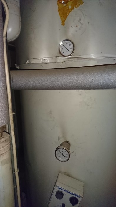Värmepanna med termometer, isoleringskanal och en del rost eller slamavlagringar på ytan.
