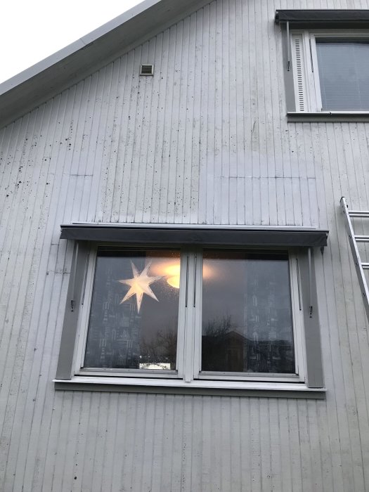 Fasad av hus med ett fönster och en julstjärna inuti, synliga spår av borttagen list under fönstret.