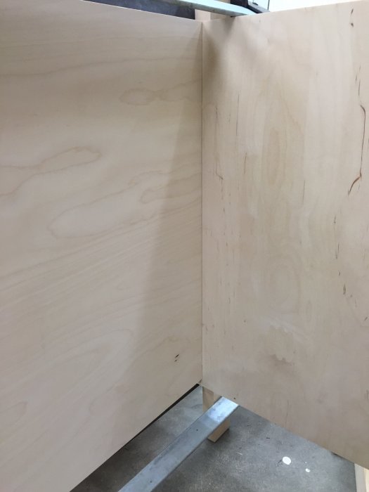 Två träplankor står uppställda i vinkel för limning i en verkstad.