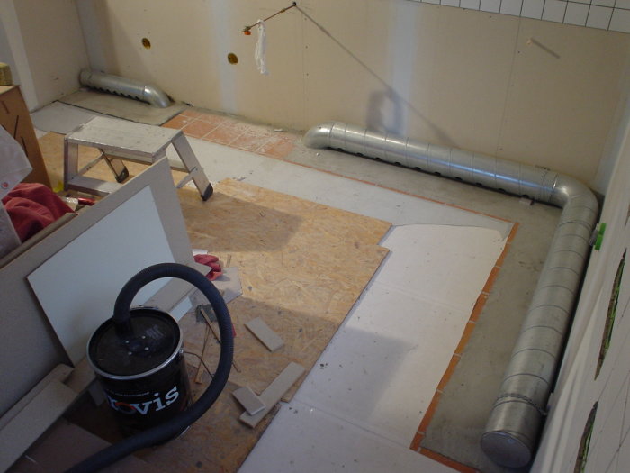 Renoveringsprojekt med synliga ventilationsrör på golv innan montering av bänkskåp.