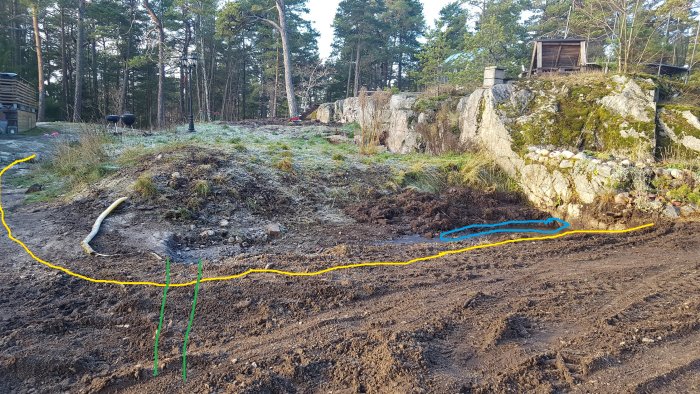 Tomt med berg och utmarkerade linjer för mur, djupaste del och dränering inför planerat byggprojekt.