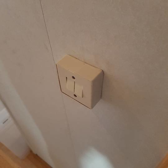 Beige dubbeltrapp brytare på spånskivevägg utan synlig dosa eller ledningsinfästning.