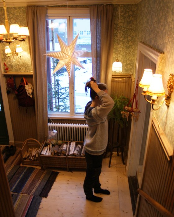 Person i gammaldags hall fäster stjärnlampa i fönster, med synligt flagnat tak.