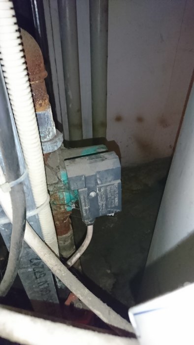 Sliten elektrisk säkerhetsbrytare monterad på en tegelvägg inomhus, omgiven av ledningar och rör.