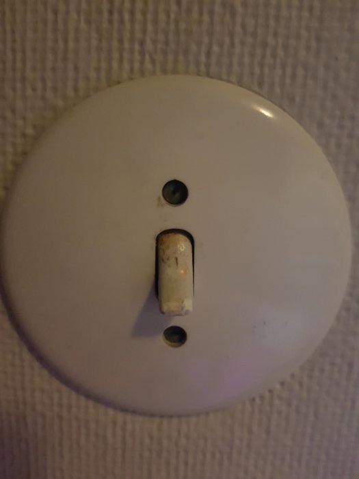Gammal vit strömbrytare från 60-talet med en trasig tändknapp uppskruvad på vägg.