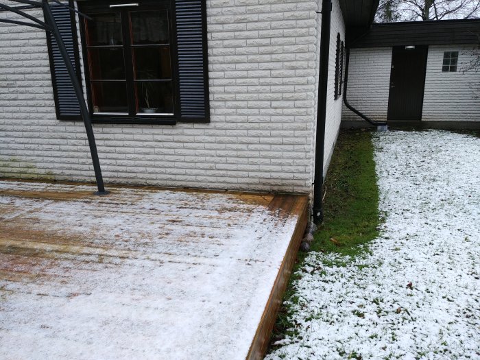 Mexitegelvägg med missfärgningar, snötäckt mark och trätrall nära huset.