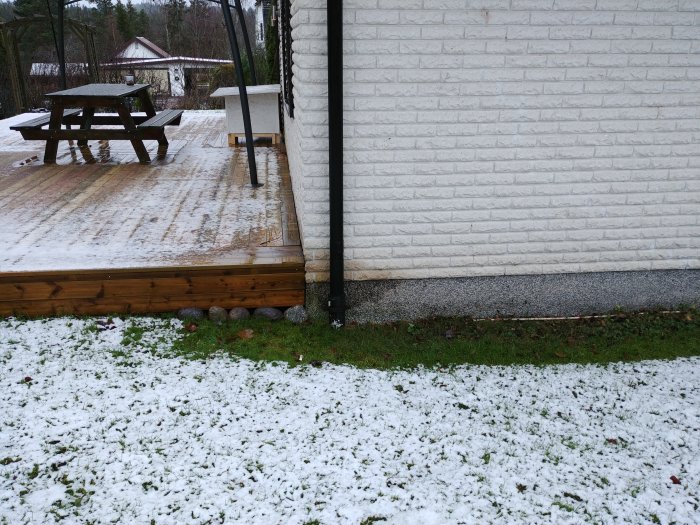 Mexitegelhus med missfärgningar vid marknivå, snötäckt gräsmatta och träterrass i förgrunden.
