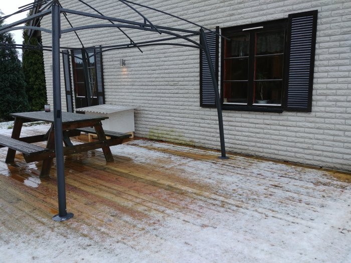 Mexitegelvägg med missfärgningar nära marken under en pergola och snötäckt mark.