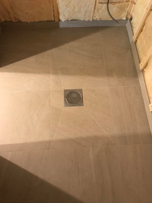 Nyinstallerad golvbrunn i ett kaklat badrum under renovering med synliga installationsdetaljer och rördragningar.