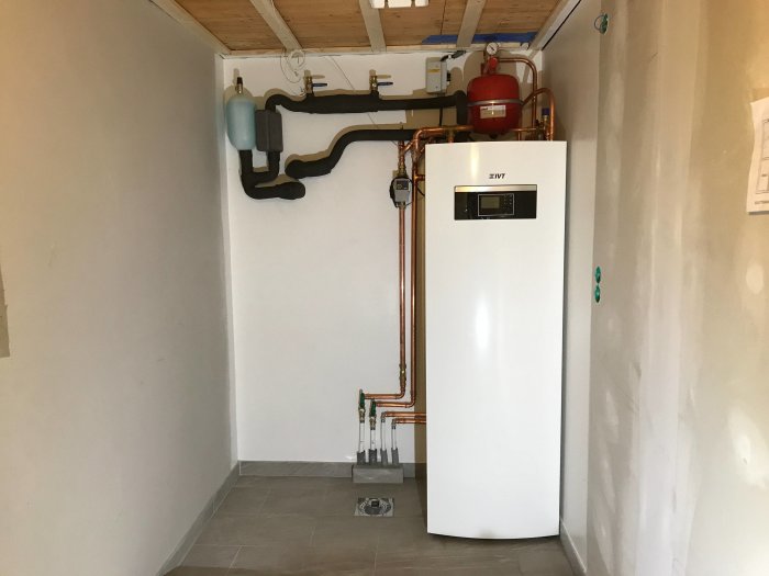 Bergvärmepump IVT Geo 312c installerad i ett renoverat rum med kopparledningar och expansionskärl på väggen.