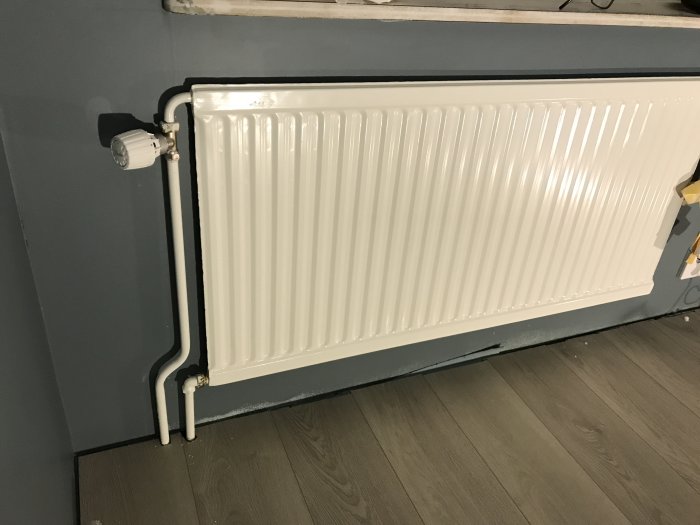 Nymålad vit radiator från Lenhovda installerad mot en grå vägg ovanför ett mörkt trägolv.