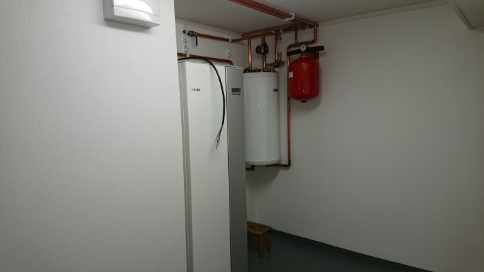 Värmepump och expansionskärl installerat på vägg med kopparledningar.