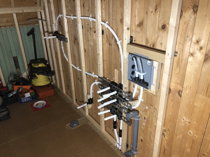 Nyinstallerade rör och rördelar längs trävägg i pågående badrumsrenovering, väntar på skvallerrör.