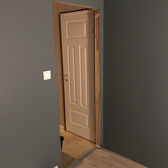 Nyinstallerad vit innerdörr med träkarm mot en mörkgrå vägg i ett hem.