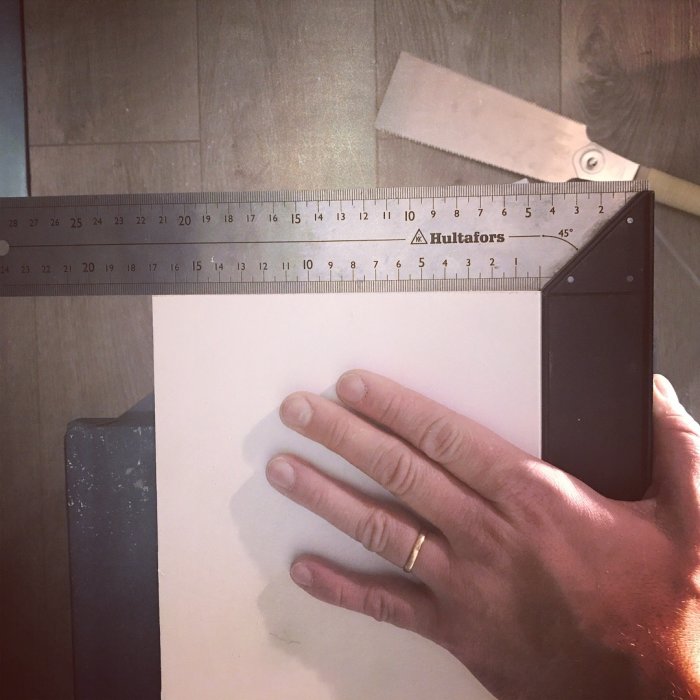 Hand mäter en vit dörrpanel med en svart T-vinkel och tumstock.