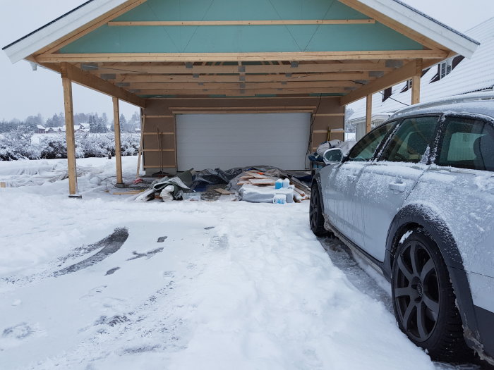 Nytt garage med öppet tak och en omonterad garageport under snötäckt landskap med bil i förgrunden.