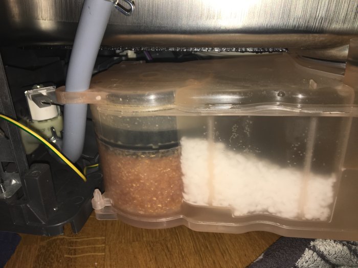 Öppen diskmaskins vattentank med salthållare, sidovägg visar orange innehåll bredvid saltet, misstänkt smuts eller filter.