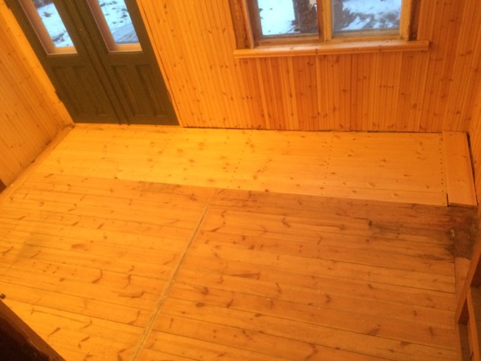 Träpaneler och golv i en hall med fönster som visar snö utanför.