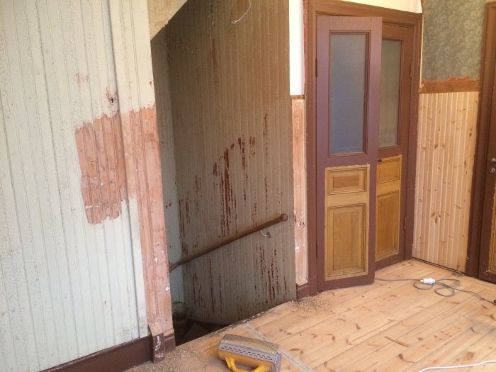 Renoveringsarbete i en hall med avskrapad tapet, en ommålad dörr och en golvslip.