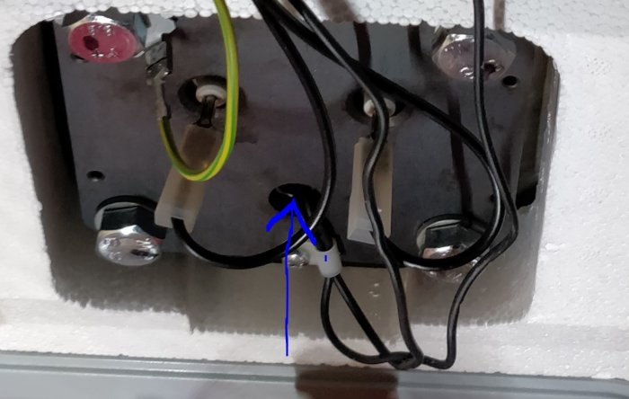 Interiör av uppvärmningsutrustning med fokus på ett mittersta rör indikerat med en blå pil, omgivet av elektriska anslutningar.