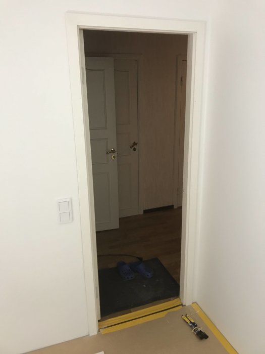 Nyinstallerat dörrfoder runt en vit innerdörr; ett par blå tofflor på golvet och verktyg vid tröskeln.