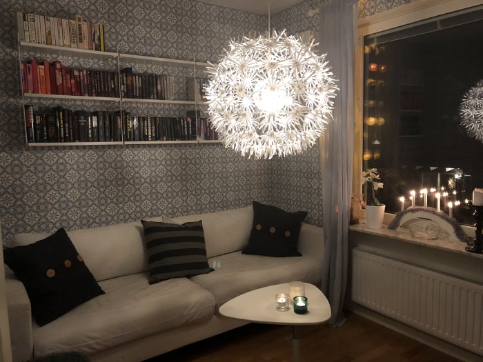 Interiör av ett TV/gästrum med bäddsoffa, String-hylla och Ikea Maskros-lampa, mysig belysning.