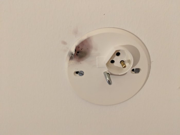 Takdoskontakt med brännmärke på locket, synliga skruvar och ingen ansluten lampa.