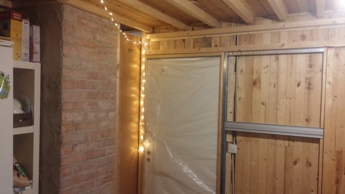 Renoveringsarbete med nytt sänkt träinnertak, spotlights planering och temporär belysning längs en plastdraperad dörr.