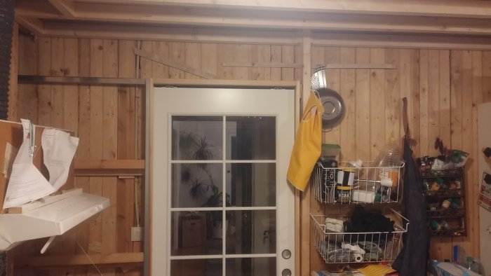 Ett kök under renovering med synliga träbjälkar, nedhängda elsladdar och en vit dörr.