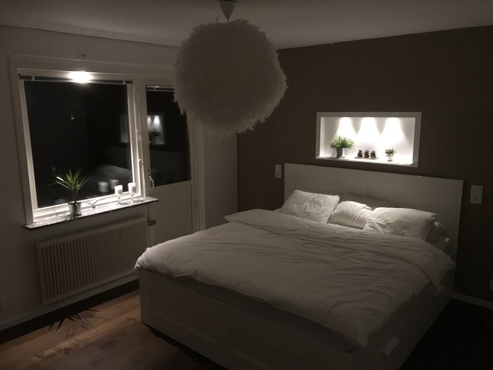 Ett halvfärdigt sovrum med en säng, fönster och hylla med belysning och växter.